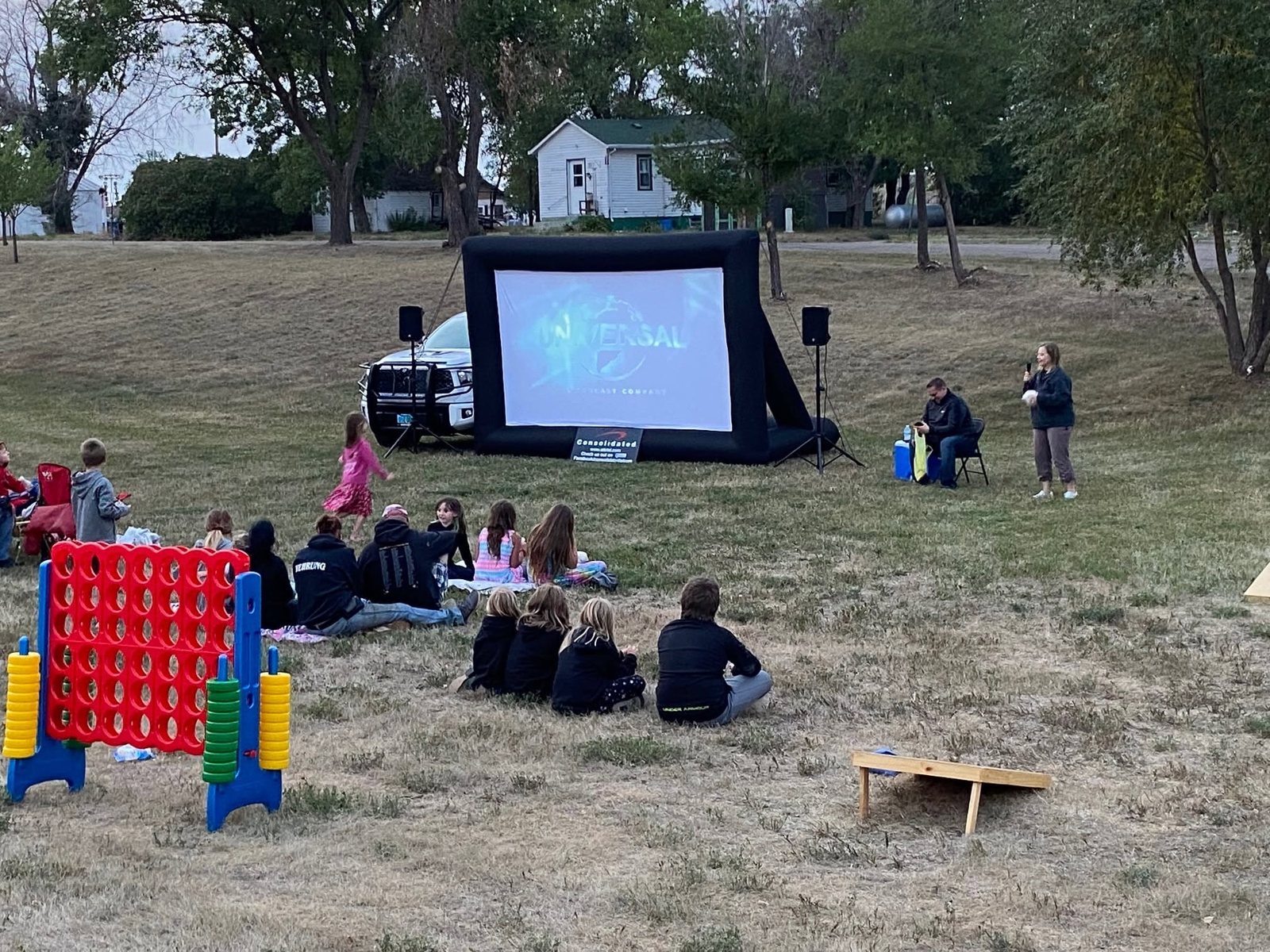 Families sitting on the grass at Dodge City Park watching an outdoor movie on an inflatable screen