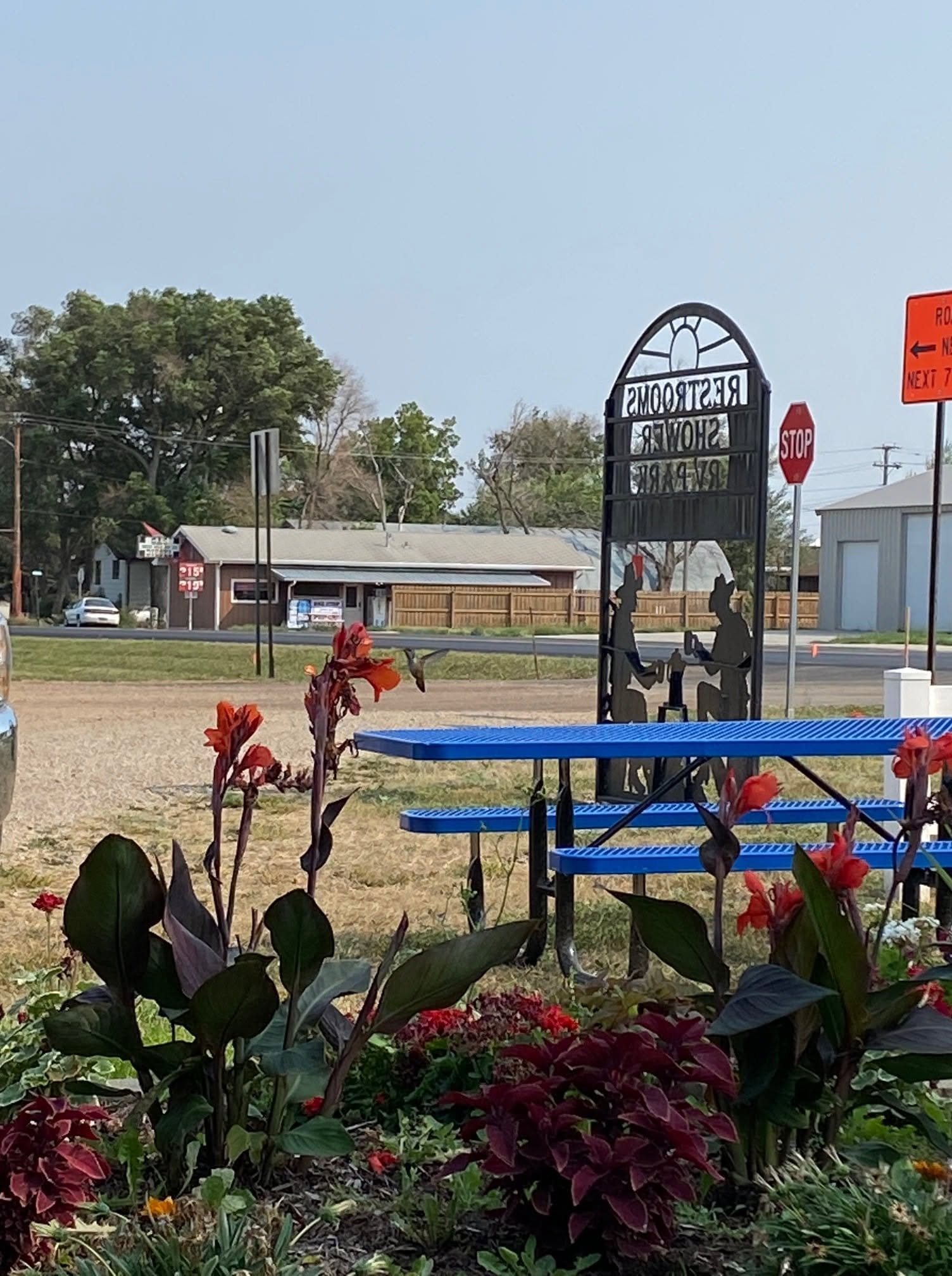 The park sign at the entrance to the Dodge city park, surrounded by red flowers and picnic tables
